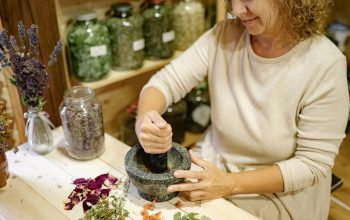 A woman using a mortar and pestle to prepare herbs in a rustic indoor setting.